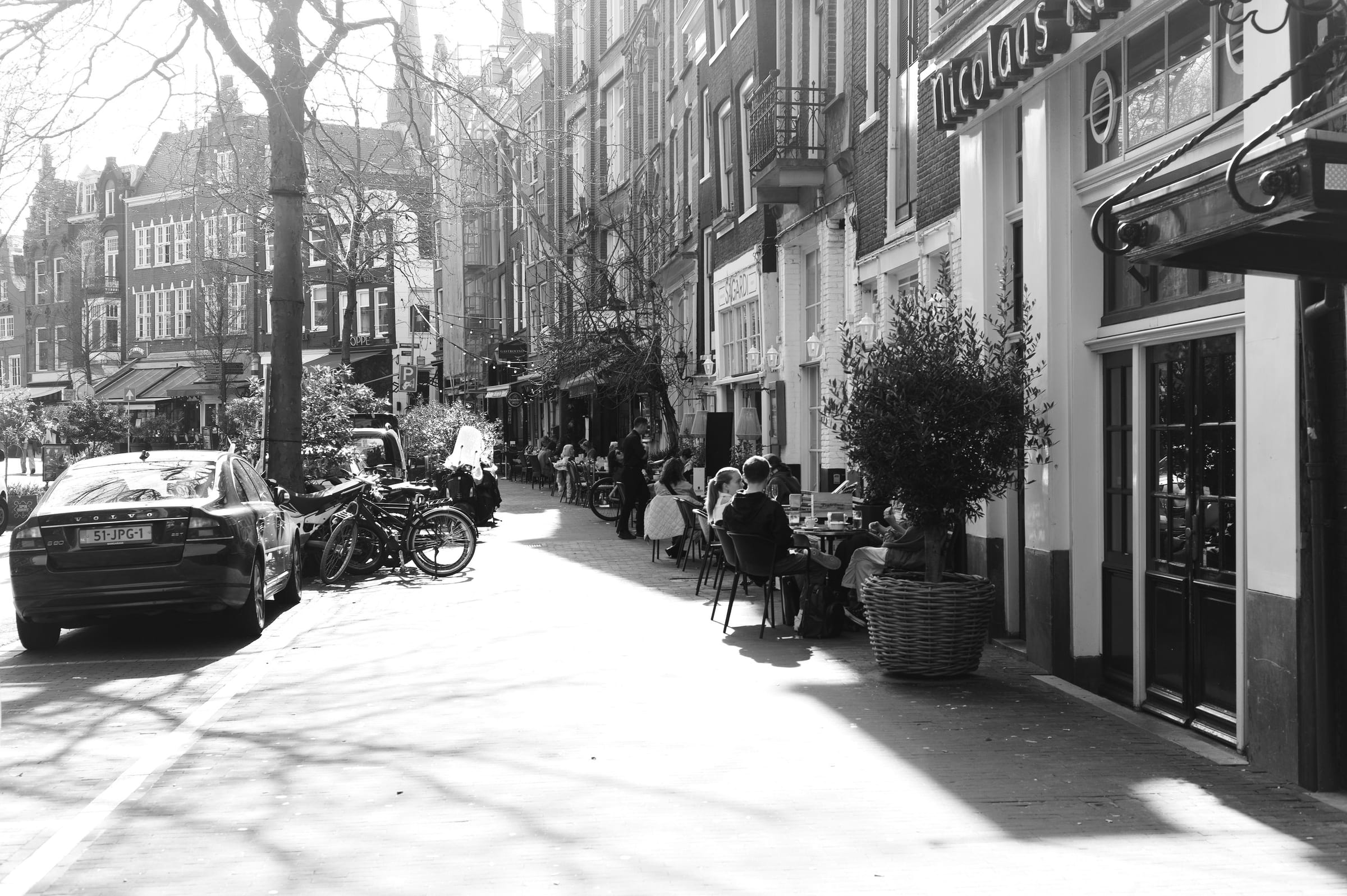 Enge Gasse mit Cafétischen im Gegenlicht, lange Schatten auf dem Pflaster