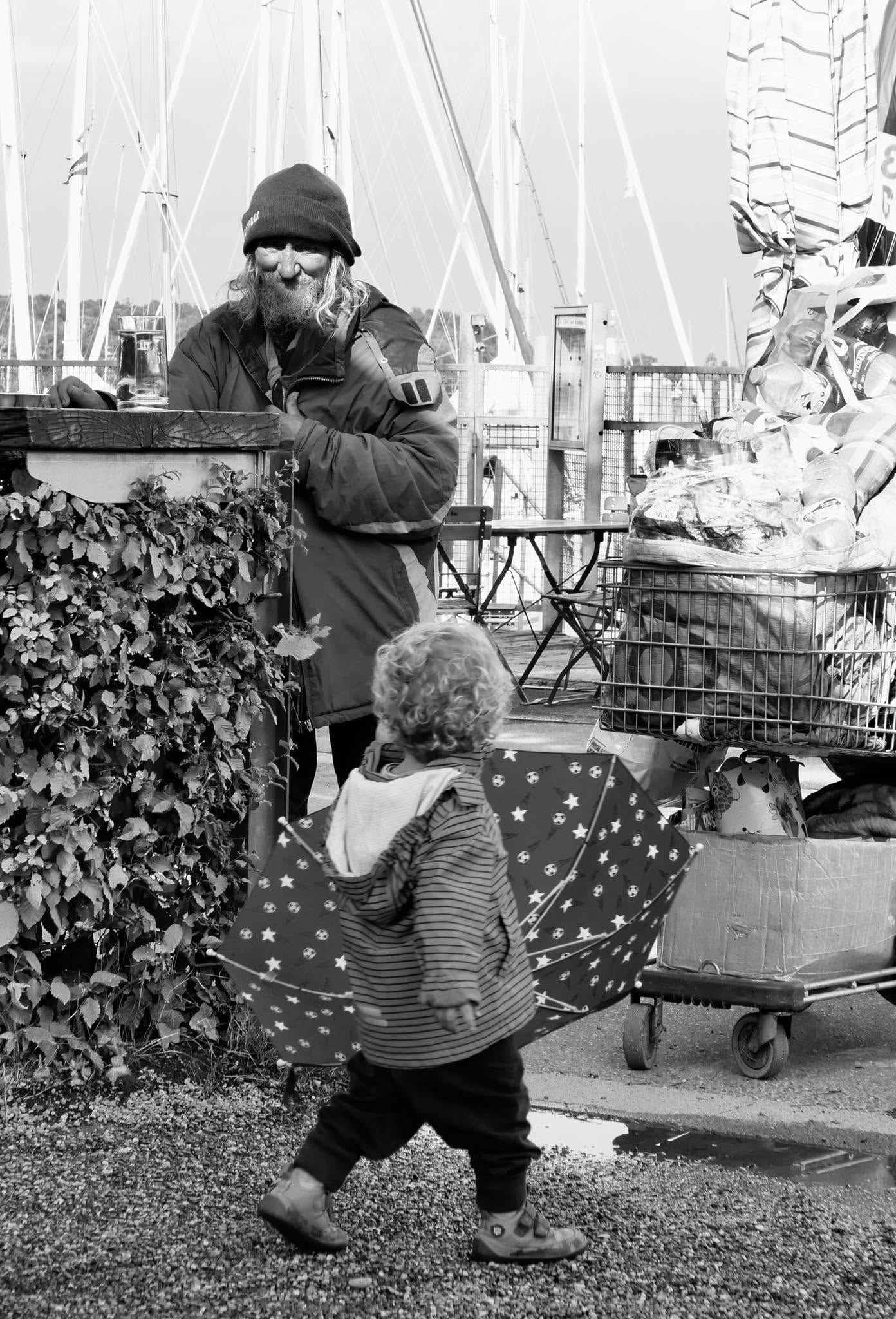 Ein Mann mit Mütze im Hafen, vor ihm ein Kind mit einem Sternenschirm