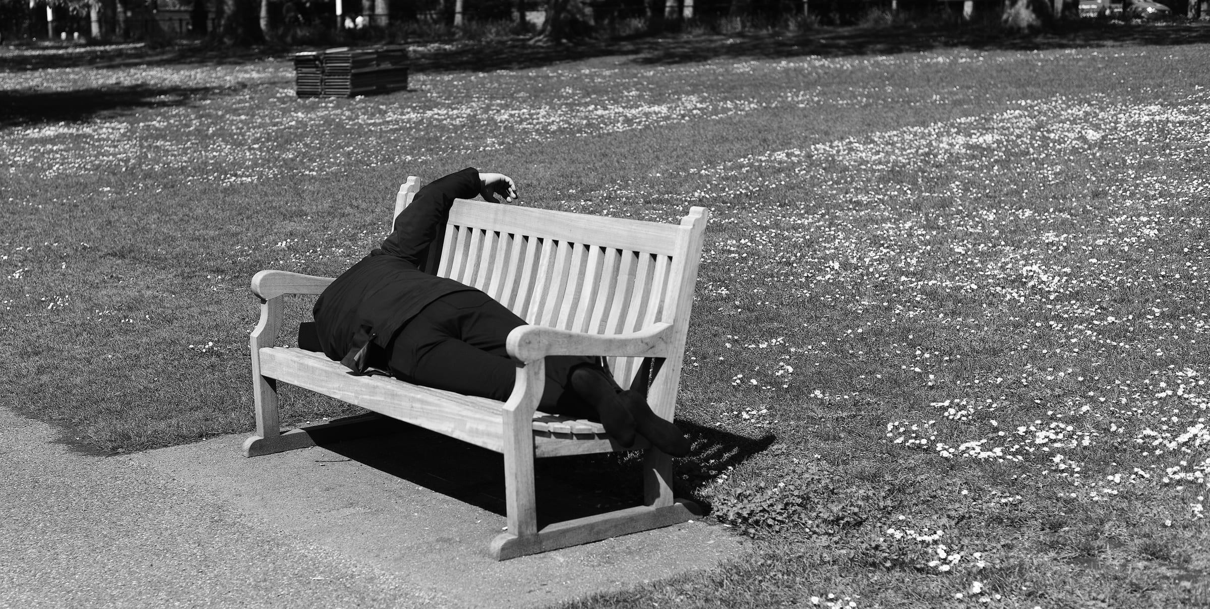 Eine schwarz gekleidete Person liegt schlafend auf einer Parkbank im Gras