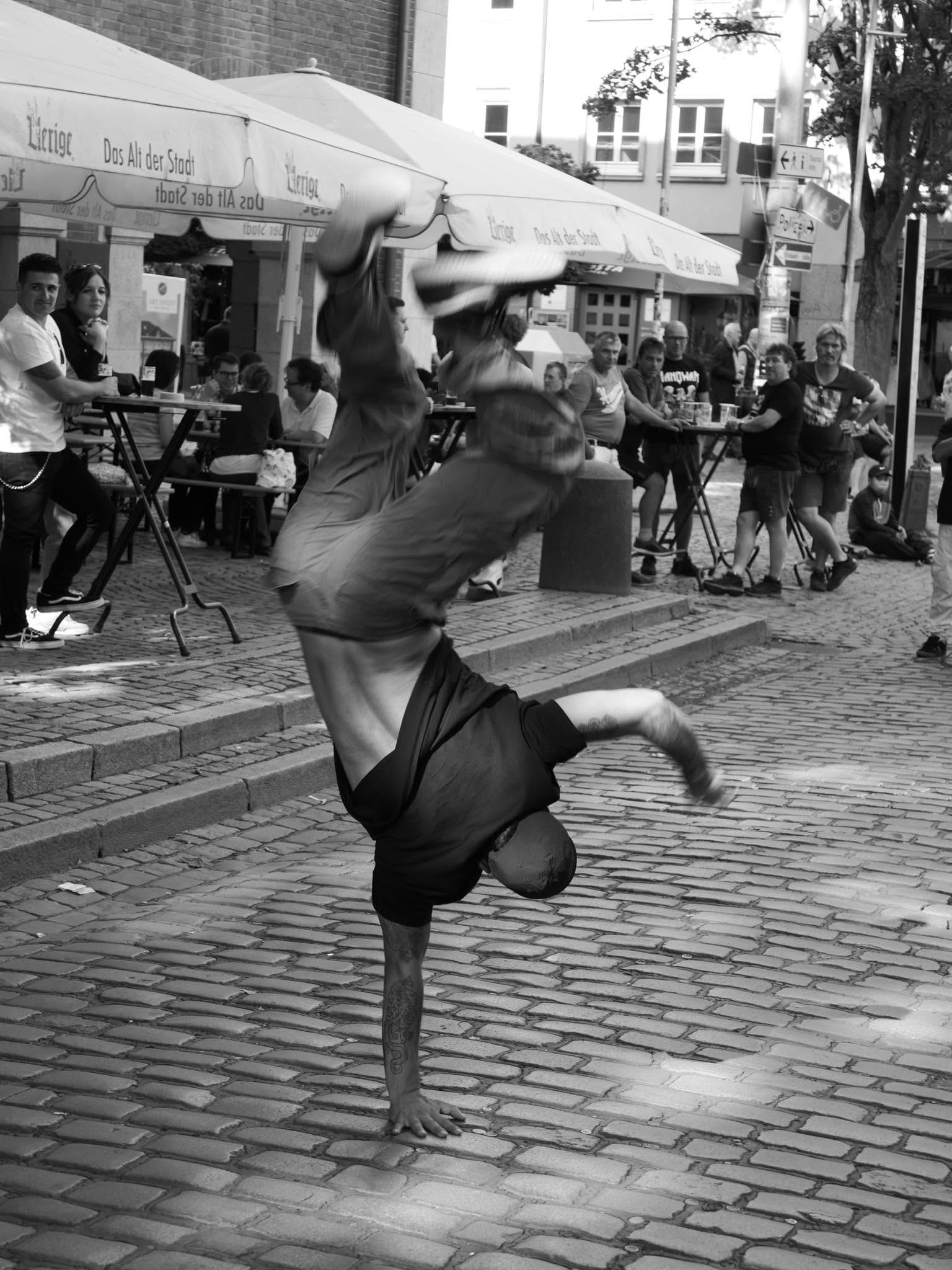 Ein Mann macht auf dem Kopfsteinpflaster vor einem Café einen einarmigen Handstand