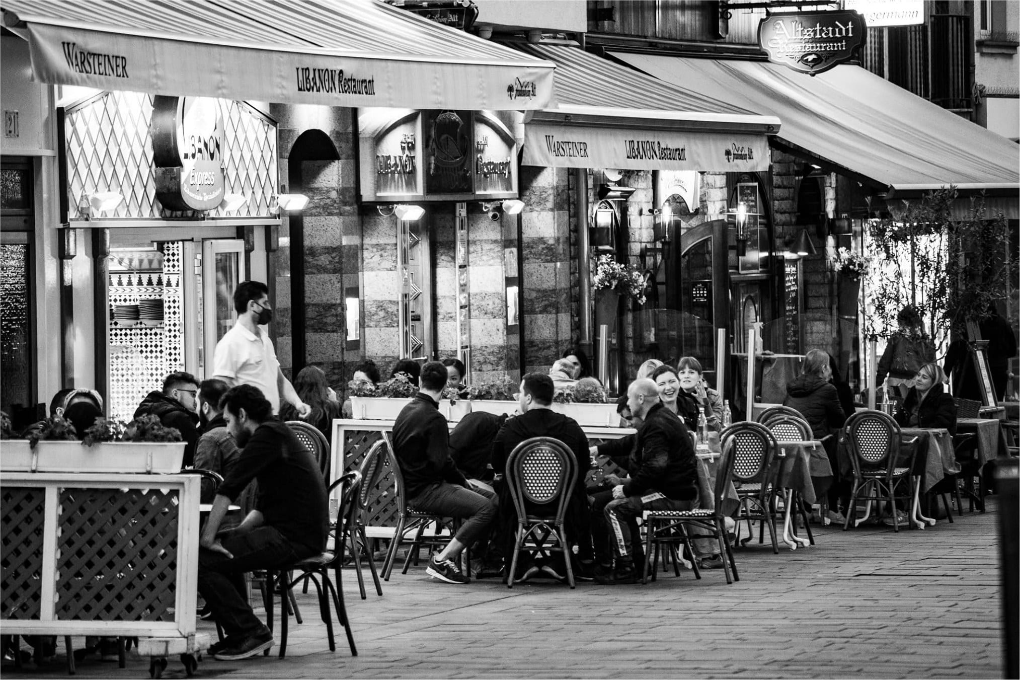 Gäste an den Tischen einer Caféterrasse unter Markisen